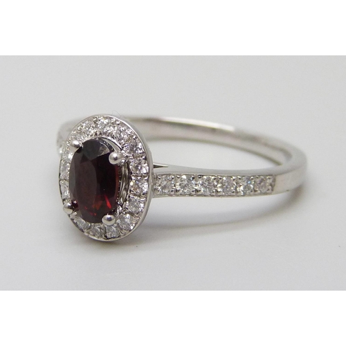 7065 - A platinum ring with an oval garnet surrounded with brilliant cut diamonds, diamond set shoulders an... 