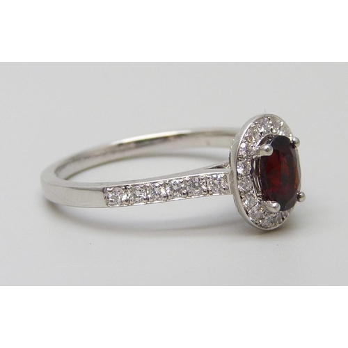 7065 - A platinum ring with an oval garnet surrounded with brilliant cut diamonds, diamond set shoulders an... 