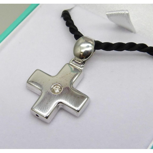 7086 - An 18ct white gold cross pendant set with 0.10ct diamond on a black cord with silver fastener, cross... 