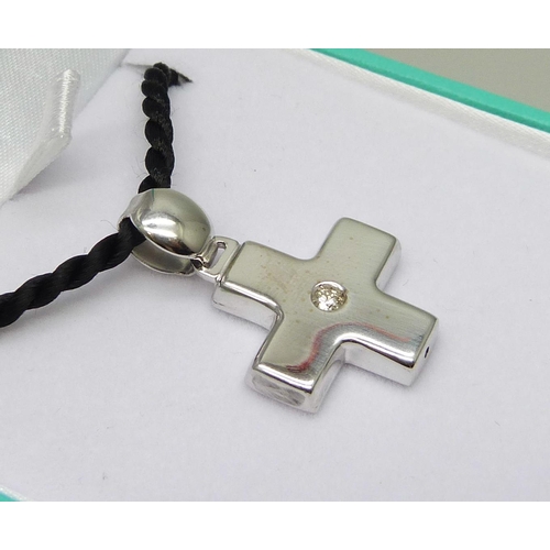 7086 - An 18ct white gold cross pendant set with 0.10ct diamond on a black cord with silver fastener, cross... 