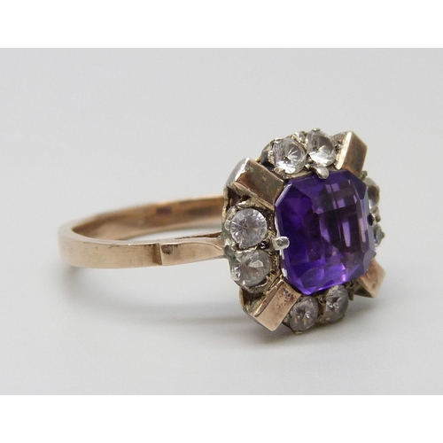 7064 - A yellow metal ring set with a central amethyst and white stones, 3g, M