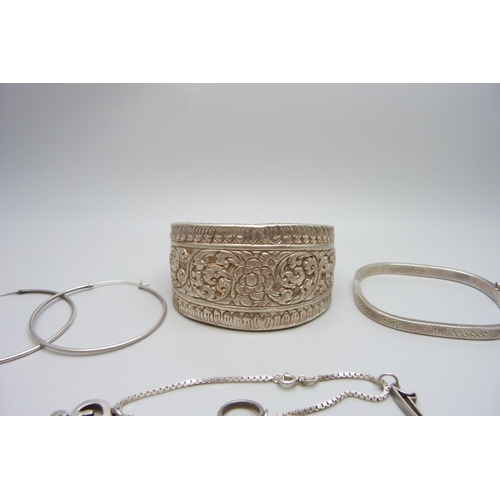 7157 - An Eastern white metal bangle, 4cm wide, a silver bracelet with charms and a pair of silver hoop ear... 