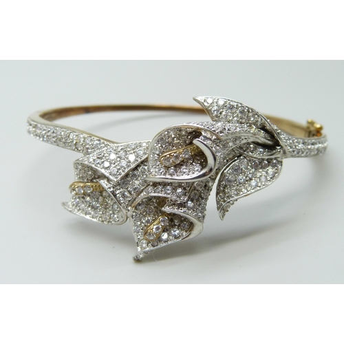 7011 - A 9ct gold bangle with white stone floral spray detail, 22g