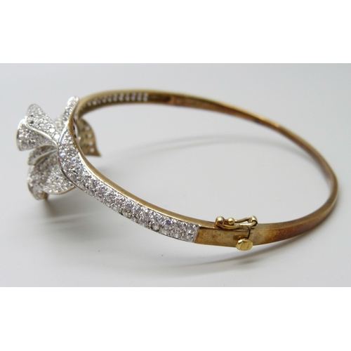 7011 - A 9ct gold bangle with white stone floral spray detail, 22g