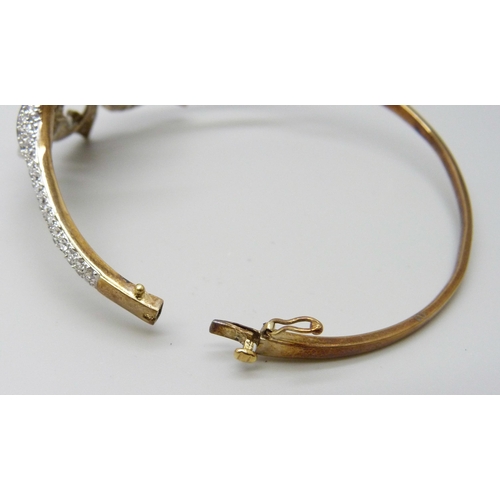 7011 - A 9ct gold bangle with white stone floral spray detail, 22g