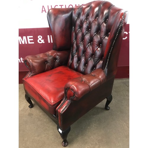 75 - An oxblood red leather Chesterfield wingback armchair