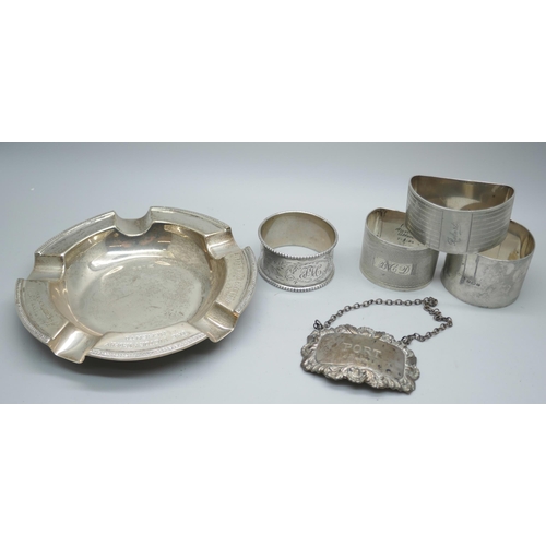 7376 - Four silver napkin rings, a silver ashtray and a silver port label, 224g