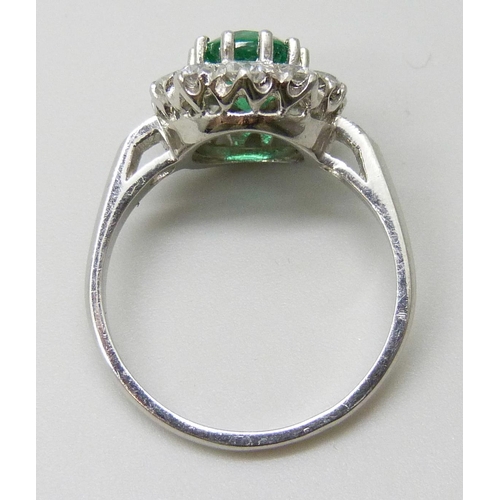 7039 - A platinum ring set with a central emerald and diamond halo and shoulders, 5.2g, N