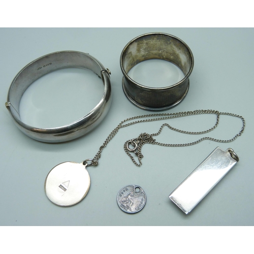 7098 - A collection of silver - a bangle, ingot, drilled coin, pendant on a white metal chain, and a napkin... 