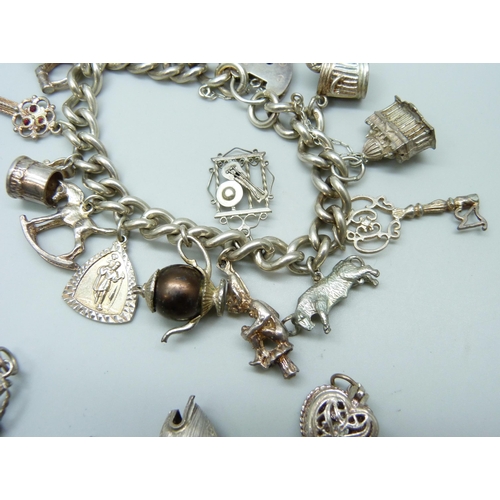 7099 - A silver curb link charm bracelet with 19 silver and white metal charms, and a white metal articulat... 