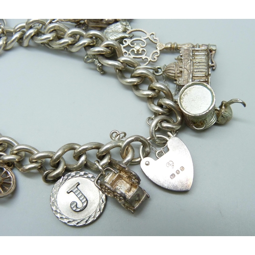 7099 - A silver curb link charm bracelet with 19 silver and white metal charms, and a white metal articulat... 