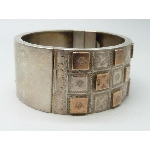 7102 - A Victorian white metal bangle with applied gold decoration, 36g, 4.7 x 5.7cm, 2.5cm wide