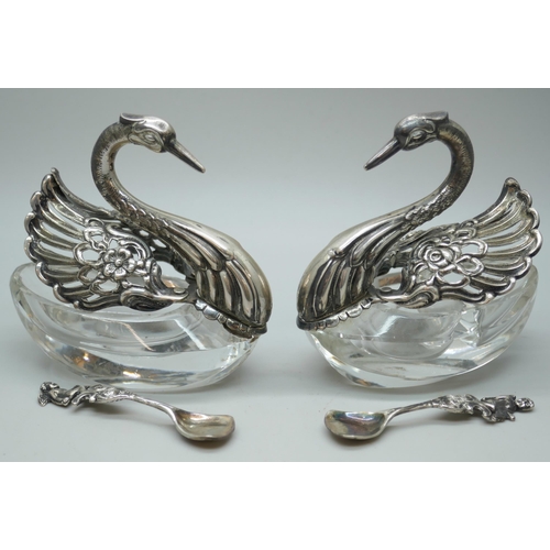 7260 - A pair of silver and glass swan salts, stamped 925, together with two silver salt spoons with cherub... 