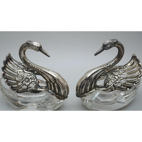 7260 - A pair of silver and glass swan salts, stamped 925, together with two silver salt spoons with cherub... 