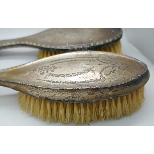 7342 - A silver backed vanity set including two brushes and an unmatched mirror, a/f