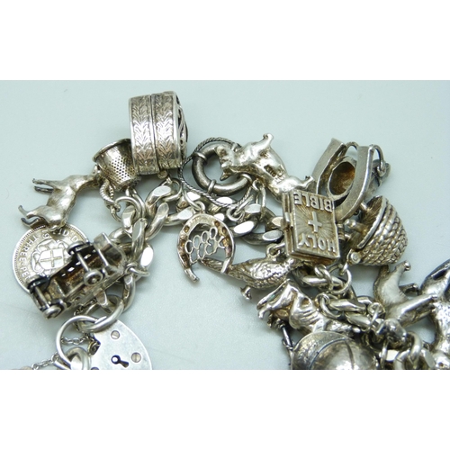 7104 - A silver charm bracelet with 27 silver and white metal charms, 109g