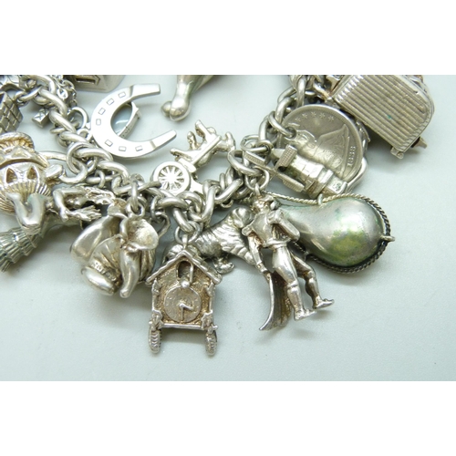 7090 - A heavy silver charm bracelet with 33 silver and white metal charms including a Georg Jensen 'Emerge... 