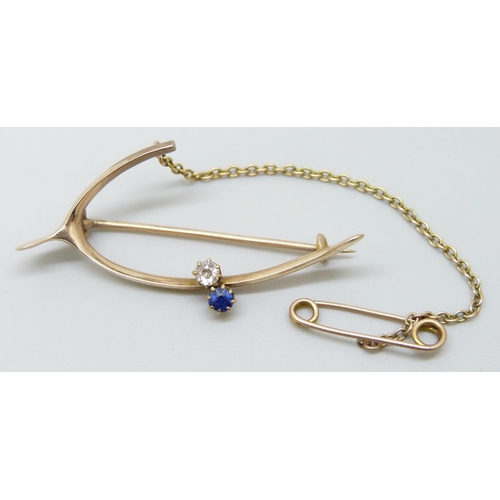 7008 - A yellow metal wishbone style brooch set with a diamond and a sapphire, 4.2g, 4.4cm