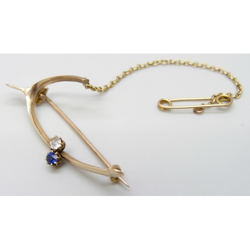 7008 - A yellow metal wishbone style brooch set with a diamond and a sapphire, 4.2g, 4.4cm