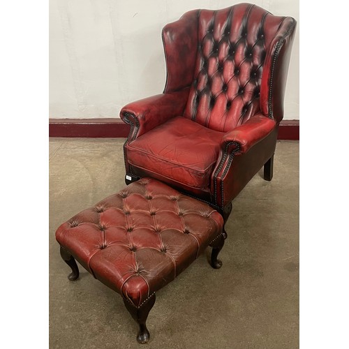 224 - An oxblood red leather Chesterfield wingback armchair and footstool