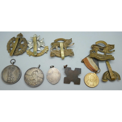 2178 - A collection of regimental cap badges, Queen Victoria medallions, etc.