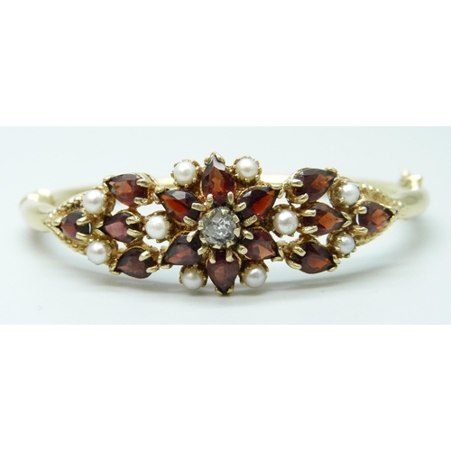 7064 - A 9ct yellow gold, garnet, seed pearl and diamond bangle, 18g