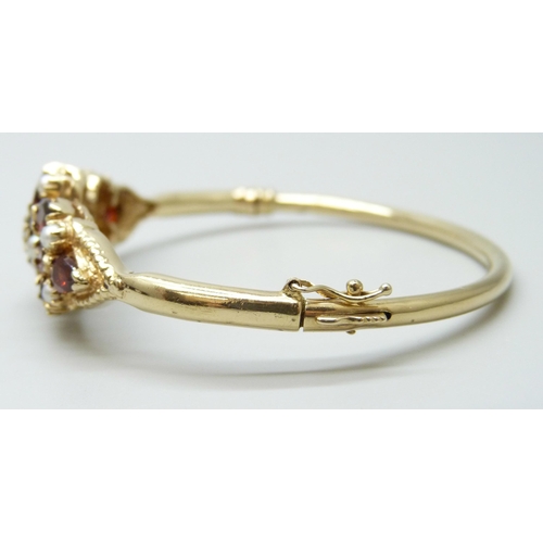7064 - A 9ct yellow gold, garnet, seed pearl and diamond bangle, 18g