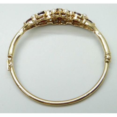 7064 - A 9ct yellow gold, garnet, seed pearl and diamond bangle, 18g