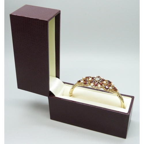 7064 - A 9ct yellow gold, garnet, seed pearl and diamond bangle, 18g