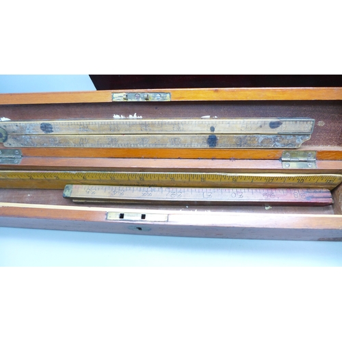 2044 - A Stanley rolling rule, boxed, two other boxes with wooden rulers, a cased set of balance scales wit... 