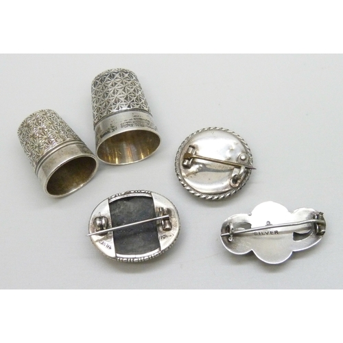 7046 - Two silver brooches, a white metal brooch, a silver thimble, and one other thimble, 27g total