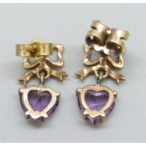 7011 - A pair of yellow metal earrings with bow detail, set with amethyst heart shape stones, 2.1g