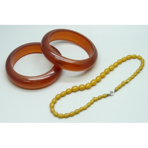 7067 - Two cherry colour bangles, and an Art Deco bead necklace with a white metal clasp, tests a silver, 9... 