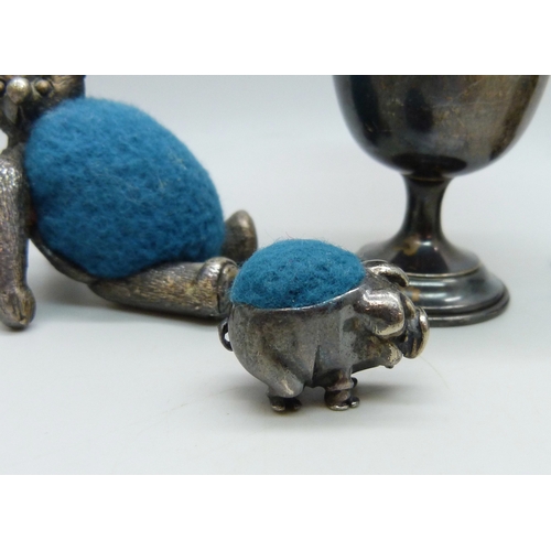 7017 - A small silver cup, 16g, a white metal pin cushion in the form of a pig, 2.5cm, and two silver plate... 