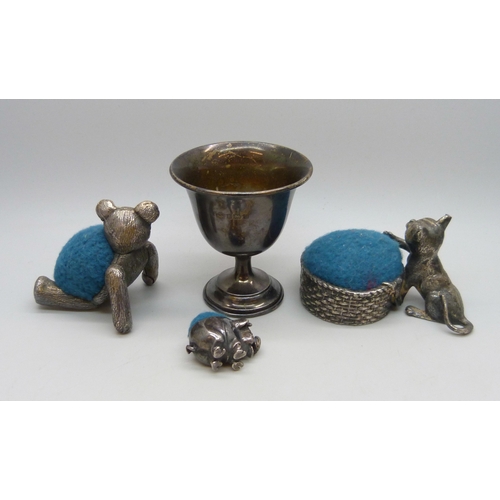 7017 - A small silver cup, 16g, a white metal pin cushion in the form of a pig, 2.5cm, and two silver plate... 