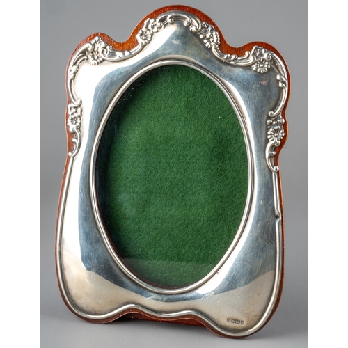 142 - An Edwardian style silver mounted oak photograph frame, the shaped silver border with embossed flowe... 