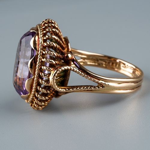 12 - A 9ct gold and amethyst dress ring, the large oval mixed-cut amethyst in rub-over settings, rope-twi... 