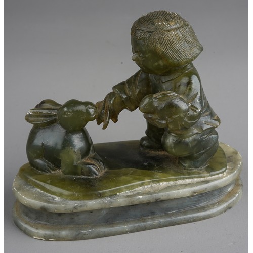 538 - A nephrite coloured carved figure of boy holding a rabbits on an oval plinth base