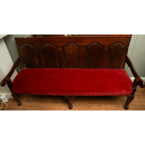 621 - A Victorian style stained oak carved settle, the back rest with geometric sections above red velvet ... 