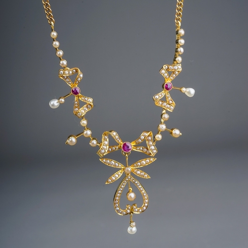 73 - An Edwardian yellow gold ruby and seed pearl necklace, three pearl-set bow motifs each centered with... 