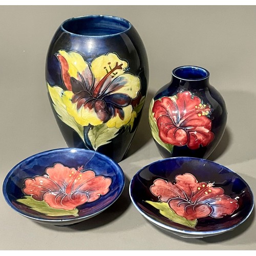 487 - Four pieces of Moorcroft pottery in the Hibiscus pattern on a dark blue ground, comprising two vases... 