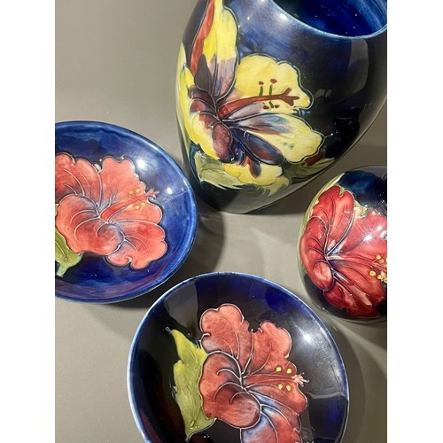 487 - Four pieces of Moorcroft pottery in the Hibiscus pattern on a dark blue ground, comprising two vases... 