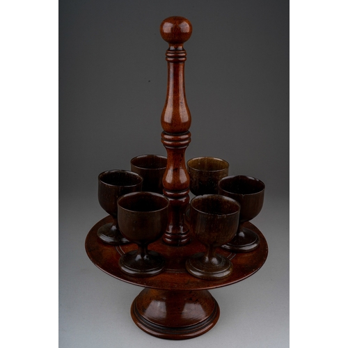 777 - An early 19th century turned treen set of six egg cups on stand, central handle, egg cups sitting on... 