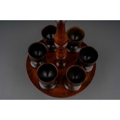 777 - An early 19th century turned treen set of six egg cups on stand, central handle, egg cups sitting on... 