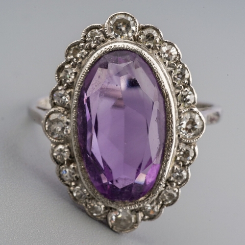 23 - An amethyst and diamond cluster ring, set with an oval shape amethyst, within a single and early bri... 