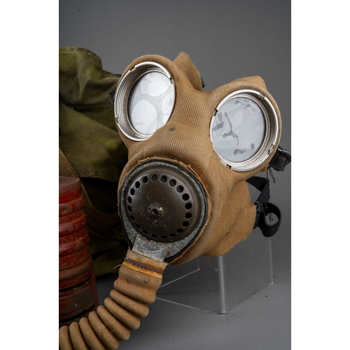 397 - A WW II gas mask, with painted red canister stamped 1940, with fabric covered face mask and tubing, ... 