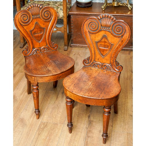 975 - A pair of Victorian oak hall chairs, the cartouche shaped back carved with coronet and scroll style ... 