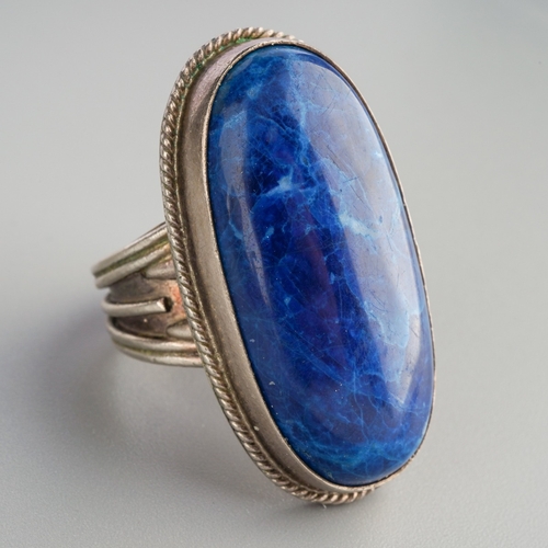 584 - A gem set ring. Set with an oval blue gemstone cabochon, rub over set within a rope twist border, re... 