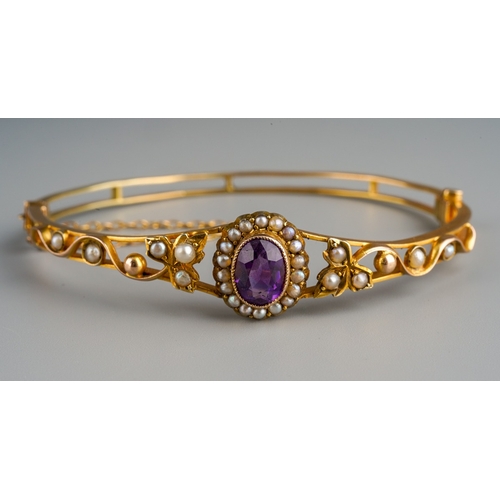 634 - An Edwardian bangle. The front set with an amethyst with seed and split pearls, inner diameter of ba... 