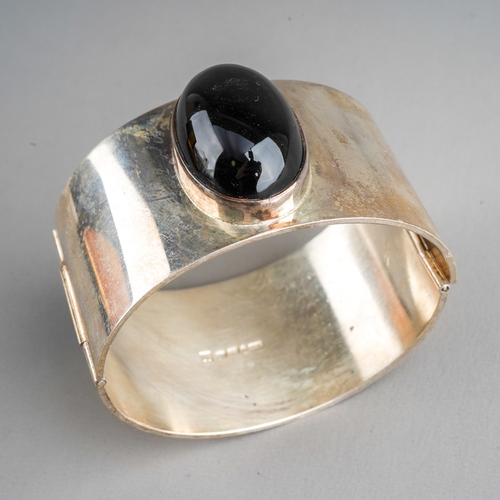 645 - A Swedish gem set bangle. The hinged bangle set with an oval black onyx cabochon, rubover set, to th... 